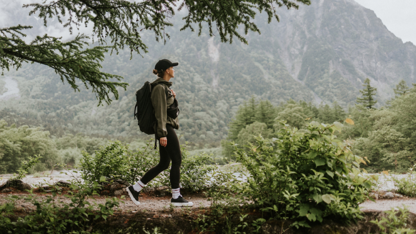 Woman walking outside in nature on a trail with mountains in the background