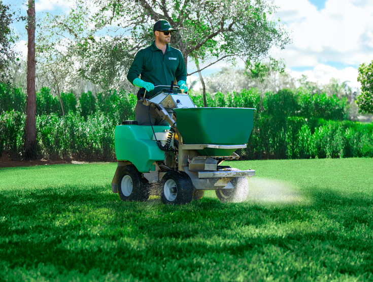 TruGreen specialist treating a lawn with a riding spreader