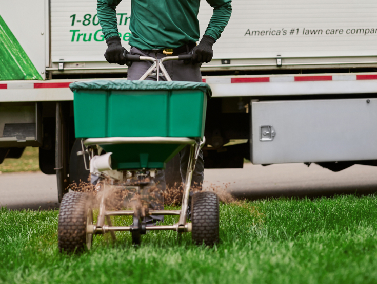 TruGreen specialist fertilizing a lawn with a spreader