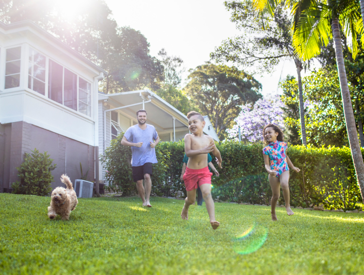 Dad and two kids running and playing on a lawn with their dog